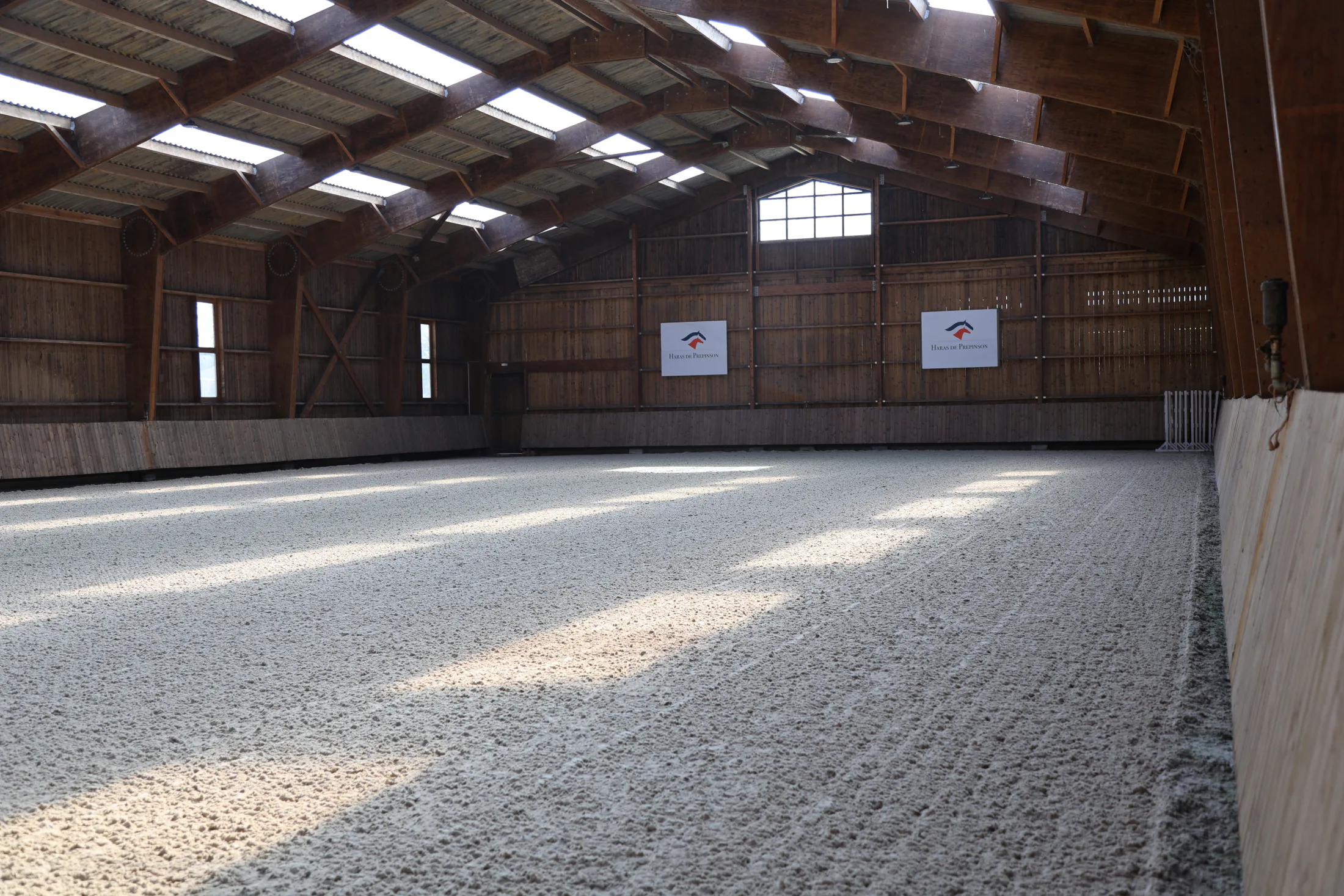 Interior of the indoor riding arena, with roof lights and a sand surface